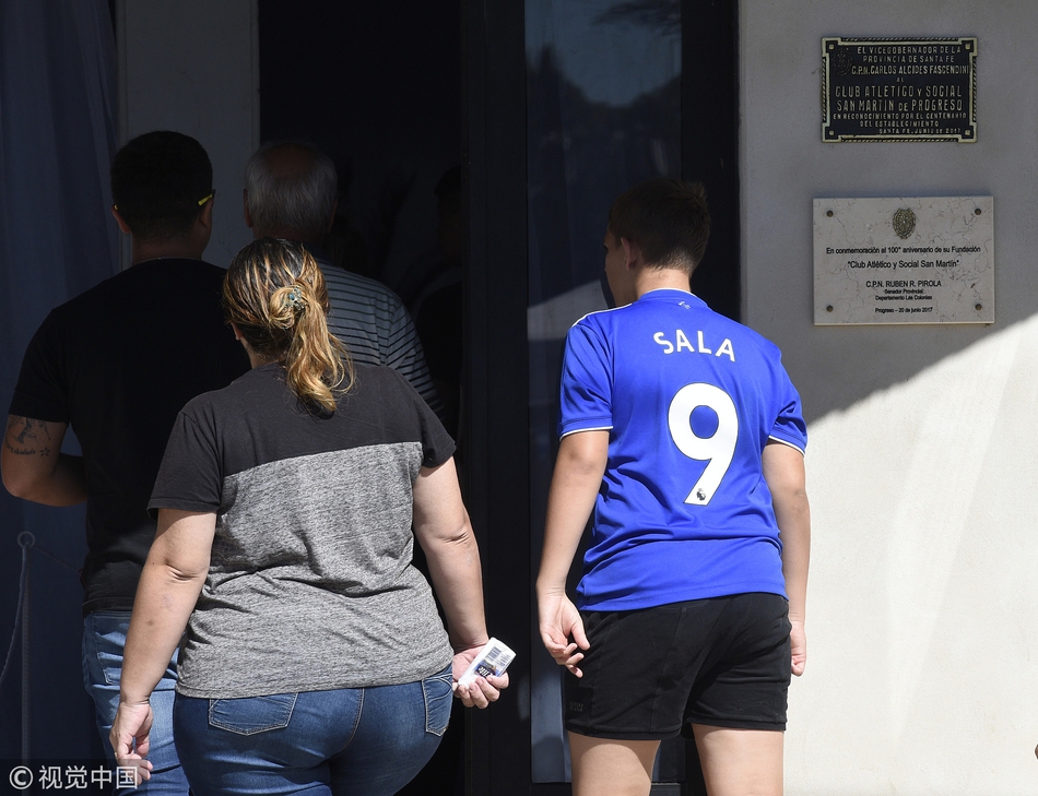 一名年轻的球迷身披阿根廷国旗，手举萨拉的球衣和照片，久久伫立在球场边。在他眼中，萨拉不仅仅是球员，更是从这片土地上走出去的英雄和永恒的骄傲。