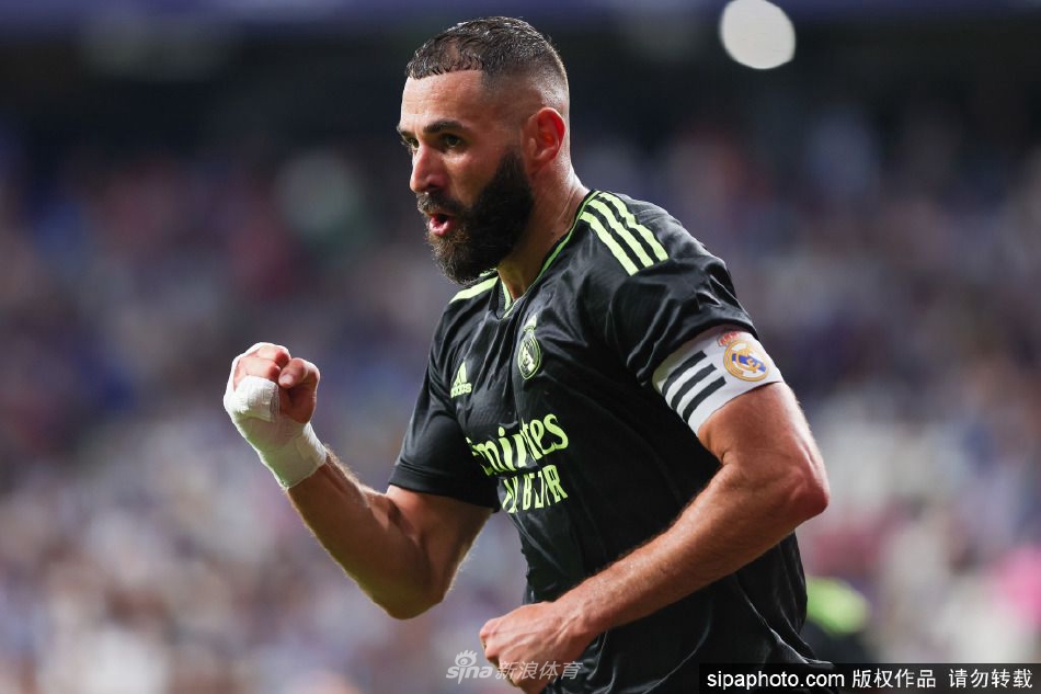 本泽马在AFE颁奖典礼上手持西甲最佳球员奖杯，面带自信微笑，身后深色幕布衬托出奖杯的熠熠光辉