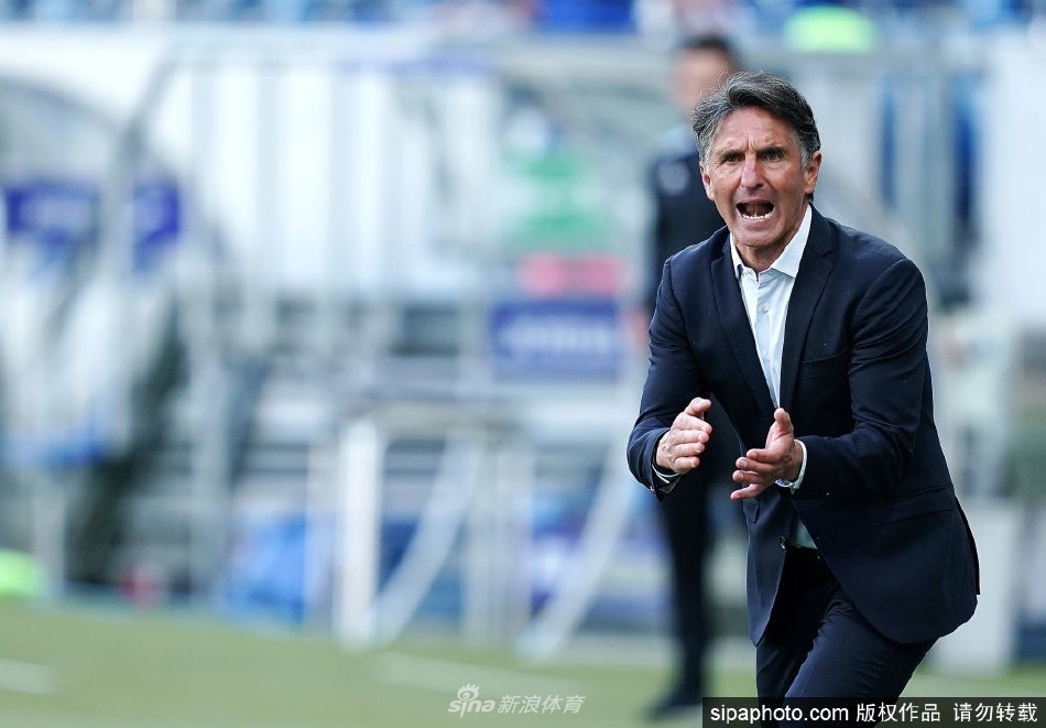 拉巴迪亚身着斯图加特训练服，在训练场上与助理教练认真探讨战术，背景是奔驰竞技场的标志性建筑