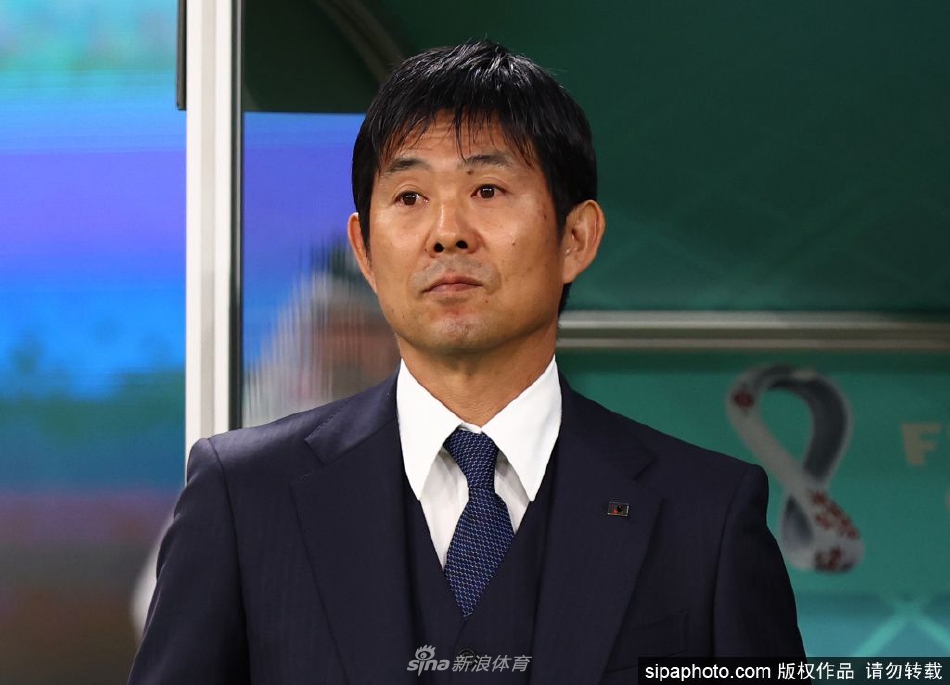 森保一在新闻发布会上面带坚定微笑，手持日本队徽足球，背景是闪烁的媒体镜头，象征着信任与新征程的开始