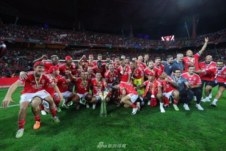 本菲卡队长奥塔门迪高举着葡萄牙超级杯冠军奖杯，奖杯在璀璨的烟花下反射出夺目光芒，周围簇拥着激动的队友，所有人脸上都洋溢着胜利的狂喜与骄傲。