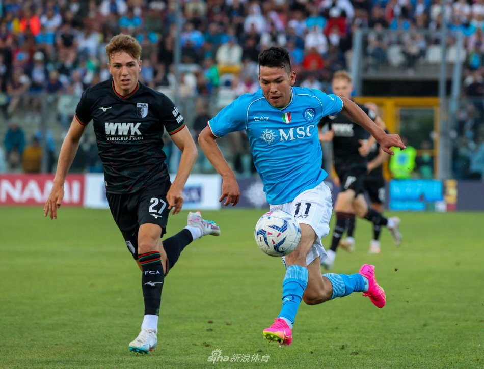 比赛精彩瞬间全景：镜头俯瞰，球场绿草如茵，双方阵型分明，皮球正在中路发展，观众席上座无虚席，气氛热烈