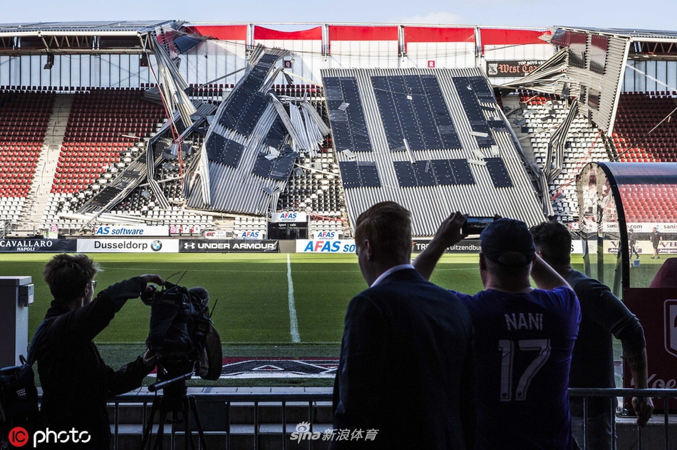 救援与调查人员在废墟中仔细勘察，身后是整排悬在半空摇摇欲坠的看台顶棚，每一根扭曲的钢架都在无声地警示着安全的脆弱。