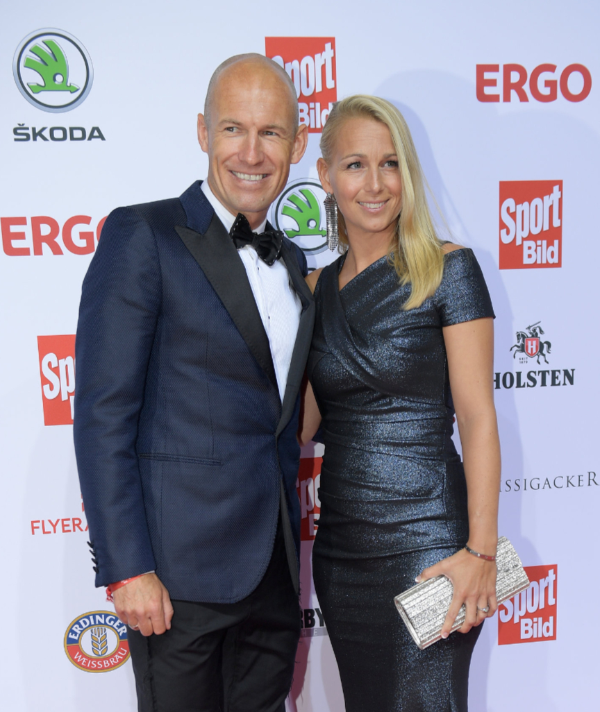 颁奖典礼近景，罗本双手紧握奖杯，胸前的口袋巾与温和的笑容相得益彰，仿佛在向支持他的球迷们致意