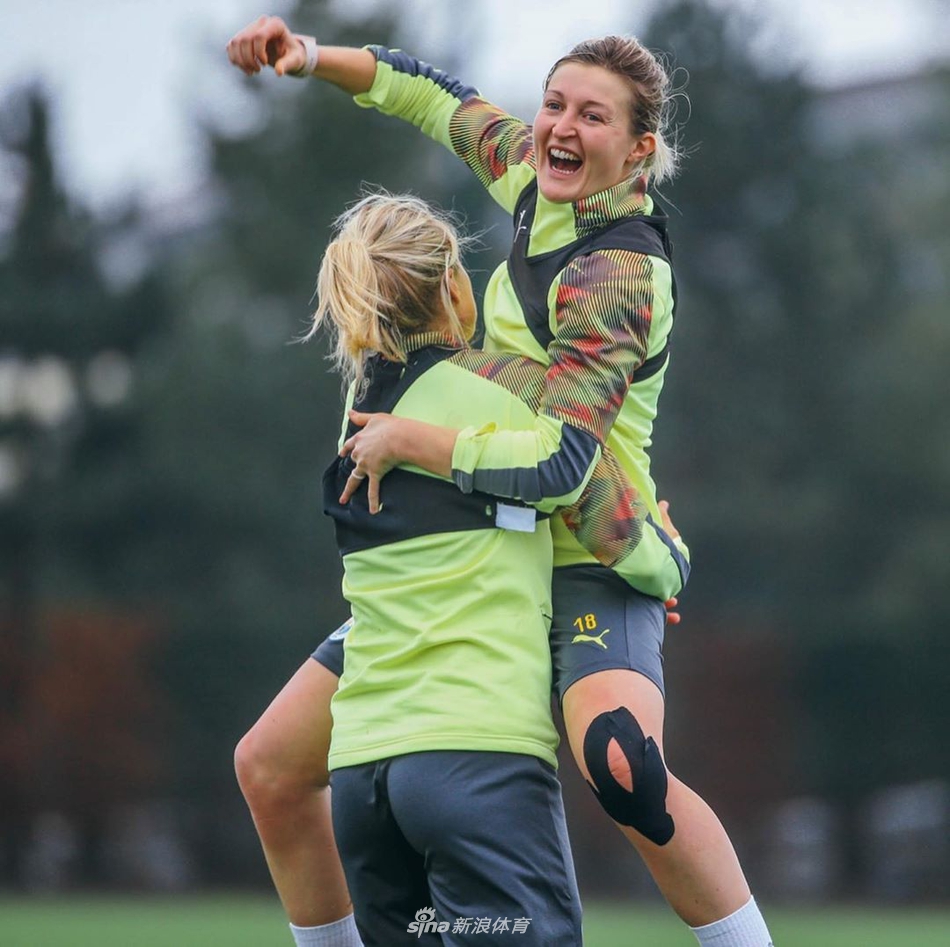 一名曼城女足球员俯身进行拉伸放松，尽管训练让她汗流浃背，但她仍对着镜头露出了灿烂而满足的微笑。