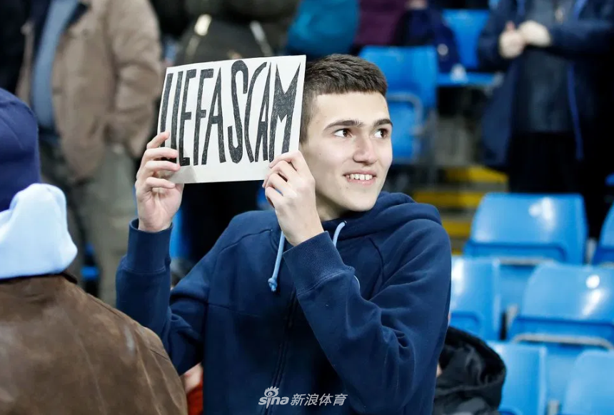 在伊蒂哈德球场看台上，一块巨大的黑布横幅格外醒目，上面用白色粗体字赫然写着“欧足联黑手党”，周围簇拥着情绪激动的曼城球迷，他们用这种方式直接而尖锐地表达着对欧足联处罚决定的愤怒与蔑视。