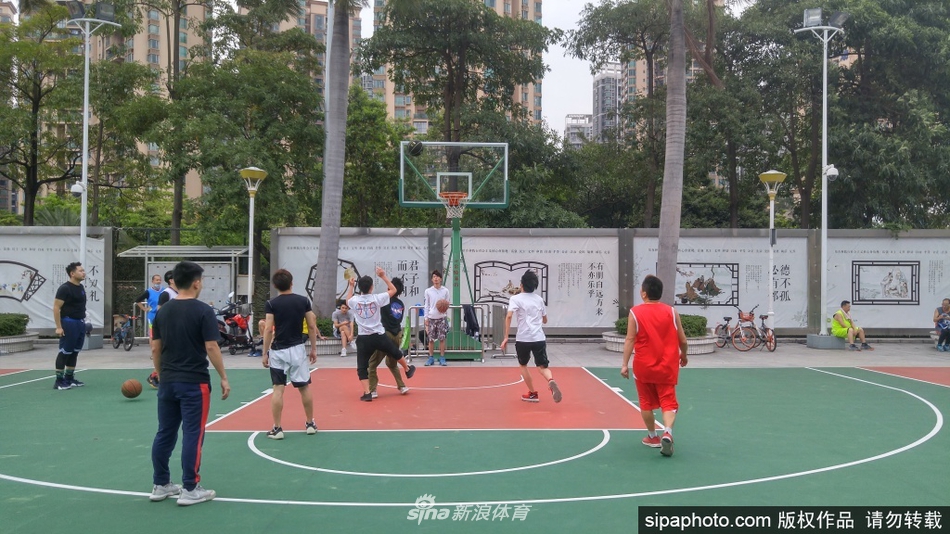 春日暖阳下,深圳宝安体育馆的蓝色篮球场上,多名身穿短袖球衣的年轻人正跳跃投篮,背景里绿树成荫,标志着运动生活正逐步恢复常态