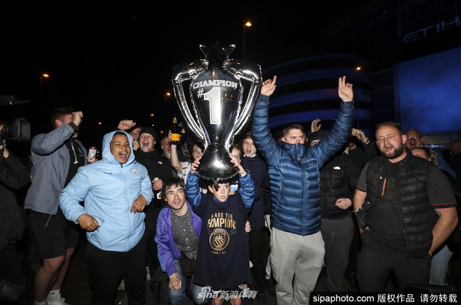 几位曼城球迷肩并着肩，对着镜头纵情高歌，他们眼中闪烁着激动的泪光，手中的围巾和横幅被高高举起，仿佛要将对球队所有的爱都倾注在这首即兴的冠军赞歌里。