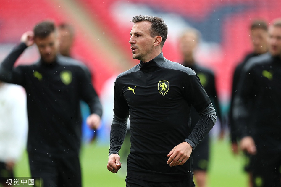 烈日当空，汗水早已湿透了球衣，但捷克队的球员们依然在进行着高强度的分组对抗。一名球员正奋力伸腿拦截，皮球在双方脚下来回争夺，战前的紧张气氛在训练场上空弥漫。