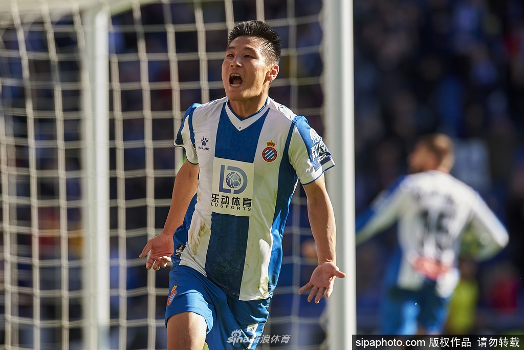 绿茵场上，几名球员戴着口罩进行着恢复性慢跑，教练员则在不远处认真观察，背景中的训练设施在阳光下投下长长的影子。