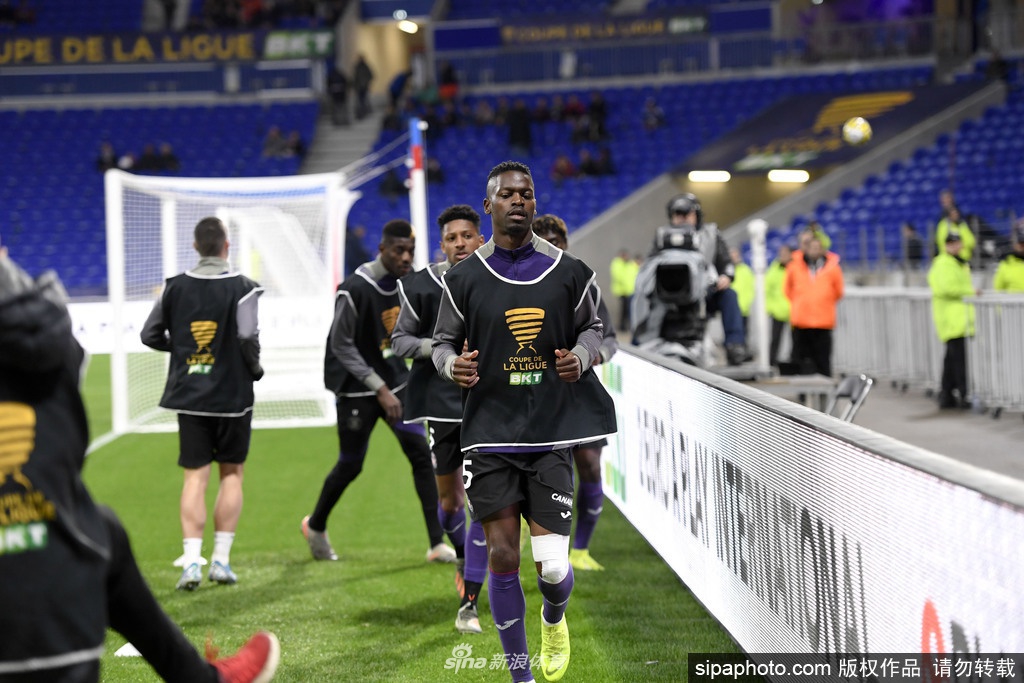 图卢兹俱乐部徽章在球场中央显得格外庄重，背景是空空荡荡的主看台，紫罗兰色的座椅在午后阳光下静默无声，诉说着降级后的冷清与即将迎来新东家的历史性时刻。