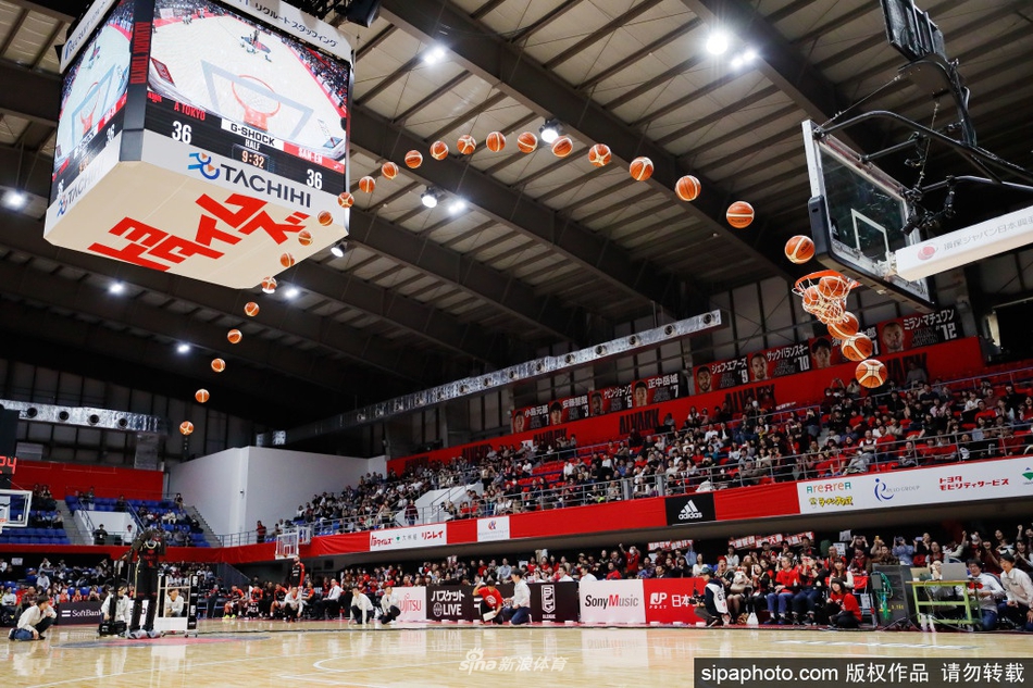 Cue机器人正在蓄力投篮，它的膝盖微微弯曲，身体重心下沉，完全模仿了人类球员的发力动作。连接在其身后基座的电缆，揭示了它作为早期型号仍需外部供电和进行定点投篮的技术特点。