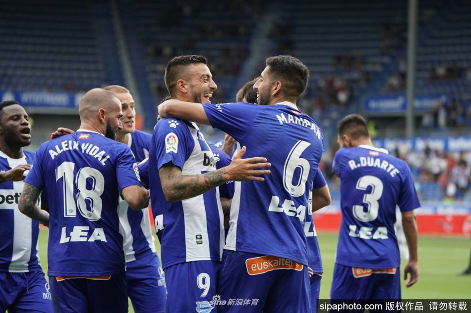 训练场上，一名穿着阿拉维斯球衣的球员独自进行着带球训练，远处是空旷的看台和稀疏的防疫工作人员，凸显了疫情时期个人与团队运动之间的微妙平衡。