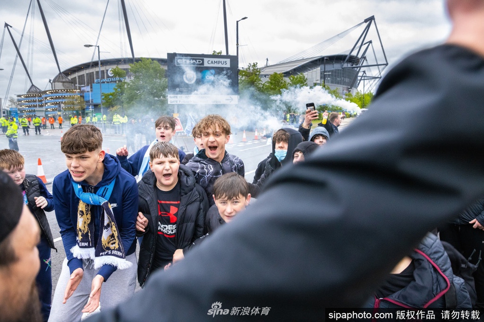 一名年轻的曼城球迷骑在父亲的肩头，脸上画着蓝色的油彩，他用力吹响手中的助威喇叭，稚嫩的眼睛里闪烁着对球队无比热爱与自豪的光芒。