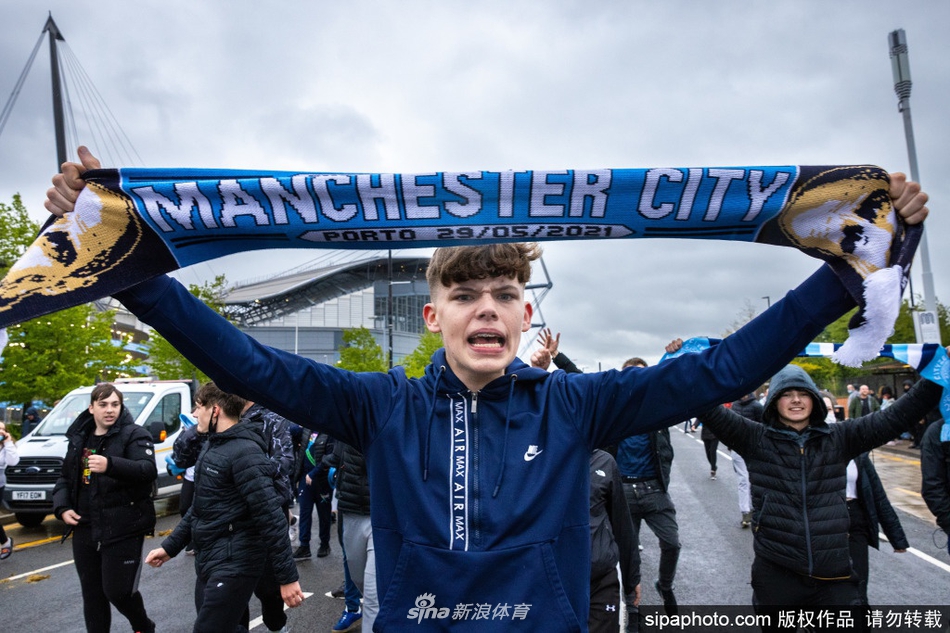 在昏暗的夜色中，蓝色的照明弹拉出长长的烟雾轨迹，一群曼城球迷簇拥在一起，对着镜头展示他们自制的印有“英超冠军”字样的横幅，每个人的脸上都洋溢着狂喜。