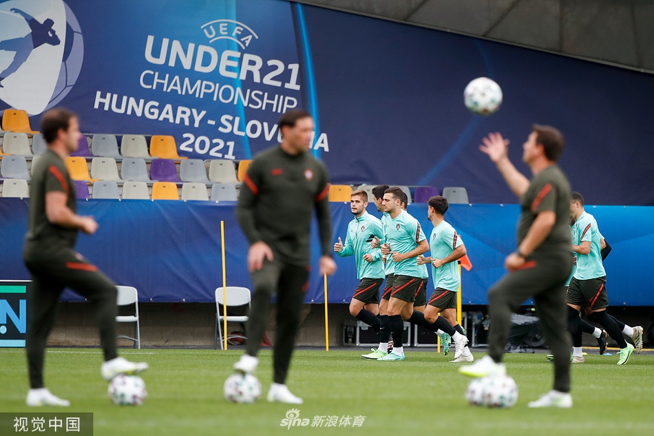 两位葡萄牙U21球员正在进行激烈的二分之一球拼抢。他们的身体几乎贴在一起，肌肉紧绷，眼神死死盯着空中的皮球。扬起的草屑和定格在半空中的水珠，凝固了训练场上最纯粹的竞争氛围，展现了年轻球员对胜利毫不退让的执着。