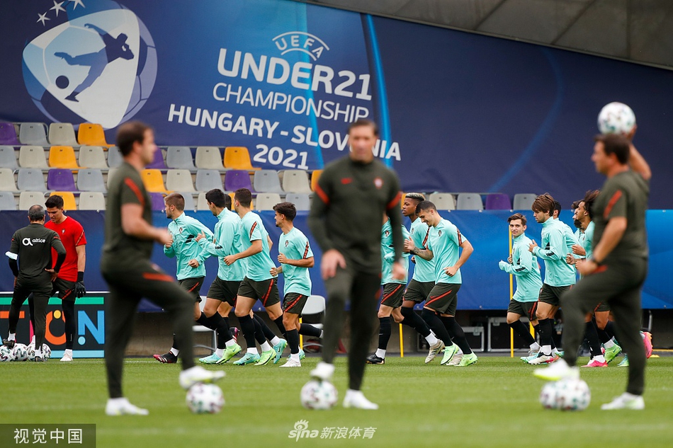 训练场上，一名葡萄牙球员正全神贯注地进行带球绕杆练习。他脚下的皮球仿佛被无形的线牵引，在标志杆间灵活穿梭，溅起的人造草屑在阳光下飞舞。远处，队友们模糊的身影和教练注视的目光，共同构成了这支青年军精雕细琢技术的生动画面。