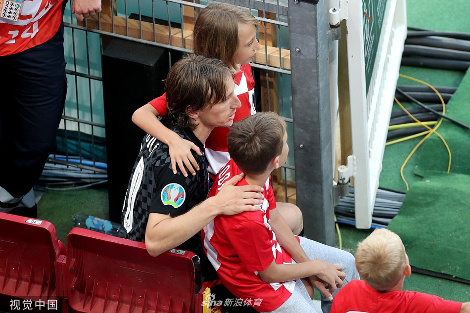 莫德里奇抱着一个更小的孩子，他温柔地注视着孩子，孩子也专注地看着他，周围的喧嚣仿佛与他们无关，只有父子间的深情对视。