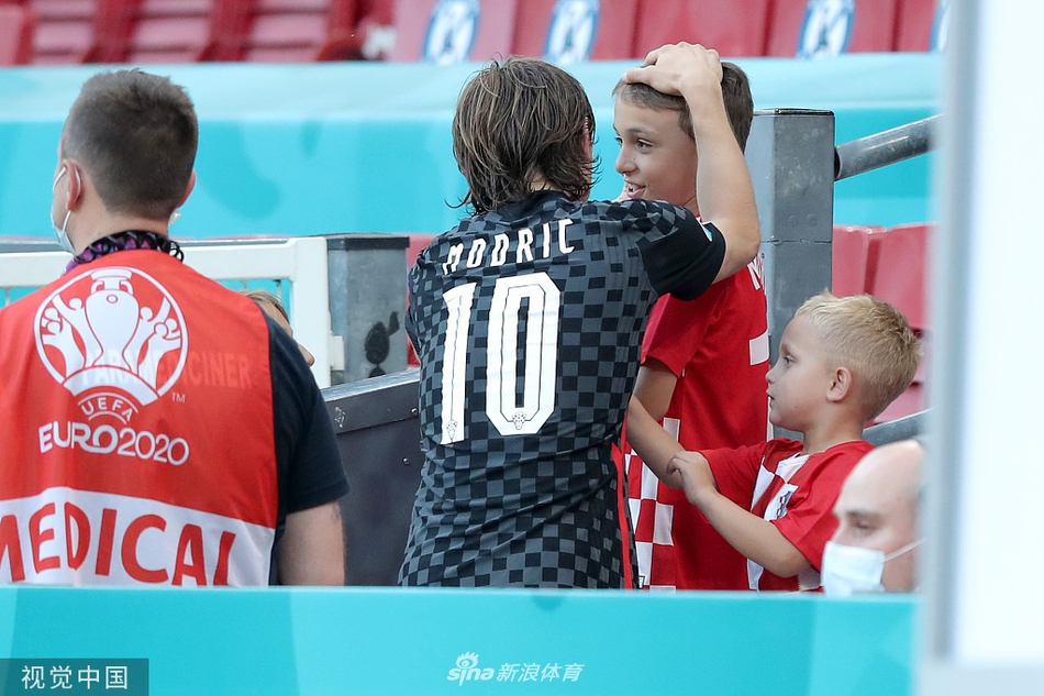 克罗地亚球员科瓦契奇赛后抱着自己的孩子在场边漫步，孩子安静地趴在他的肩头，科瓦契奇的表情从失落转为平静，享受这难得的亲子时刻。