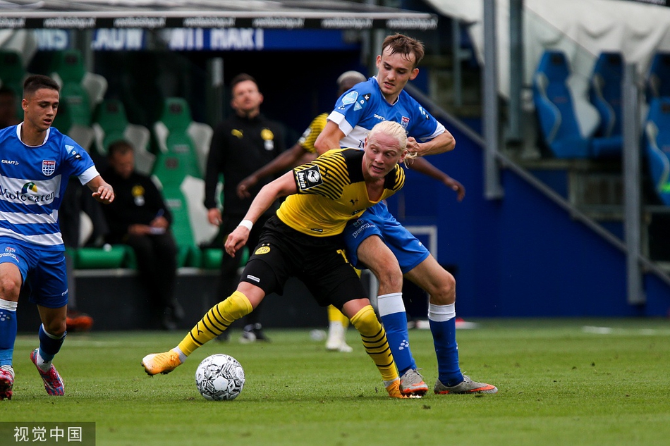 多特蒙德U23主教练在场边神色专注，他身体前倾，双手做出战术手势，向场上队员传达明确的指令，背景是荷兰特有的低地晚霞