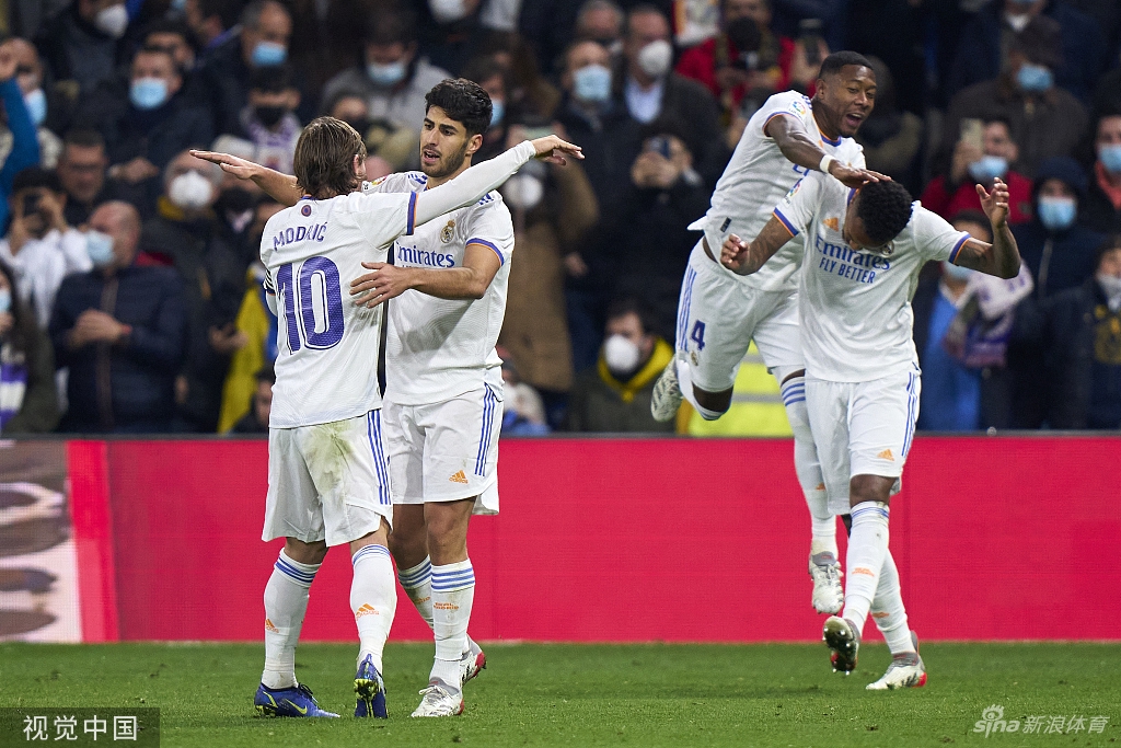 皇马球员赛后围拢在一起相互击掌鼓劲，展现出强大的团队凝聚力，背景是开始散场的伯纳乌球场，灯光璀璨如同白昼。