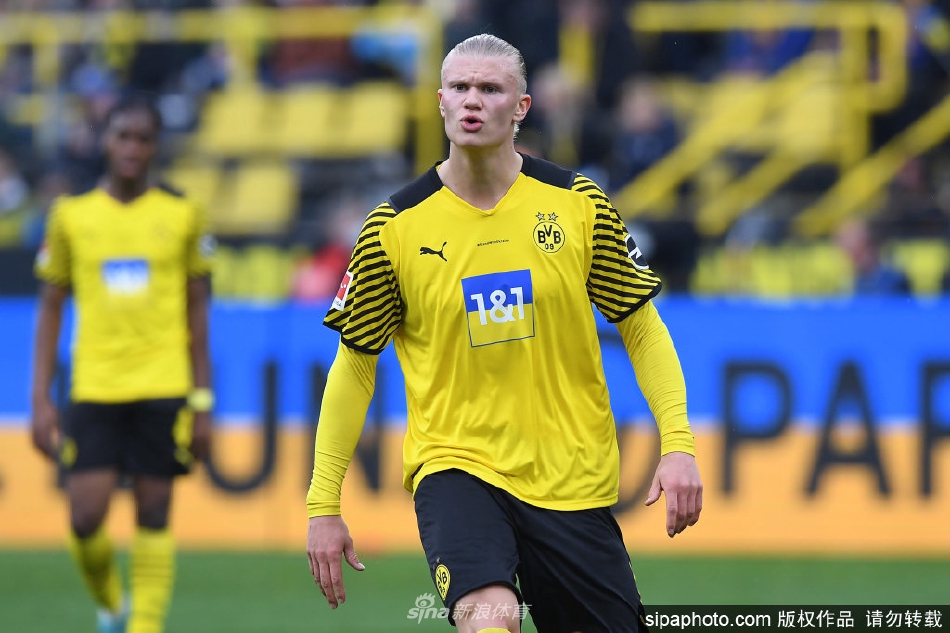 哈兰德在体检中心手持曼城围巾微笑，眼中充满了对新征程的期待与喜悦