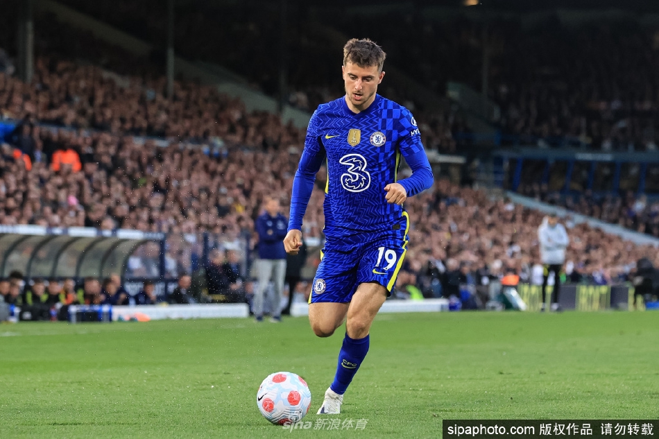 芒特身穿切尔西球衣，手指队徽向看台球迷致意，眼神中充满了坚定与归属感。