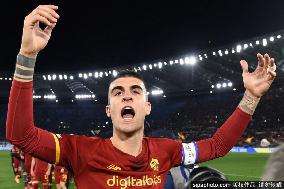 吉安卢卡-曼奇尼在新闻发布会上手持罗马球衣，面带坚定笑容，背景是俱乐部的巨大标志，象征着他对红狼军团的郑重承诺。