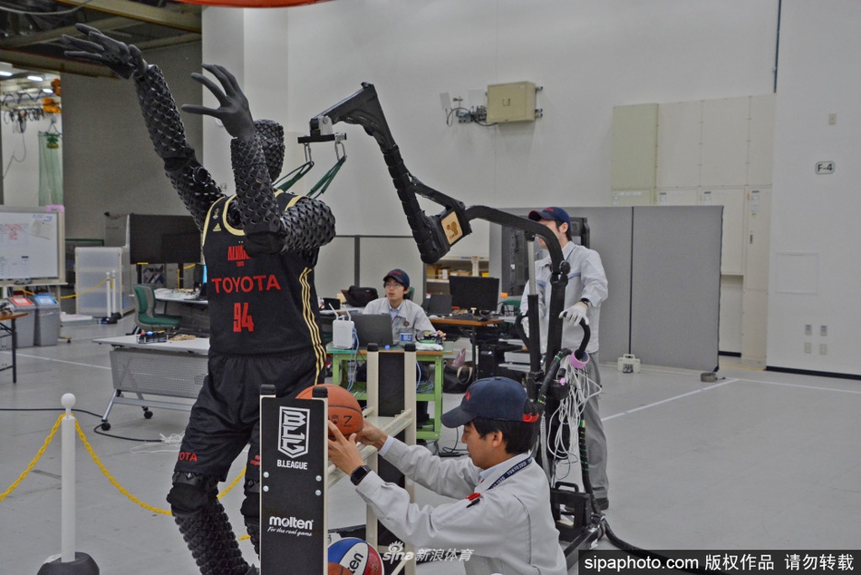 Cue4机器人正利用脚下的滑轮在球场上灵活移动，这是它进化出的全新能力。画面中，它正准备弯腰拾起地板上的篮球，整个动作流畅自然，标志着机器人从定点炮台向具备自主移动能力的‘球员’迈进了一大步。