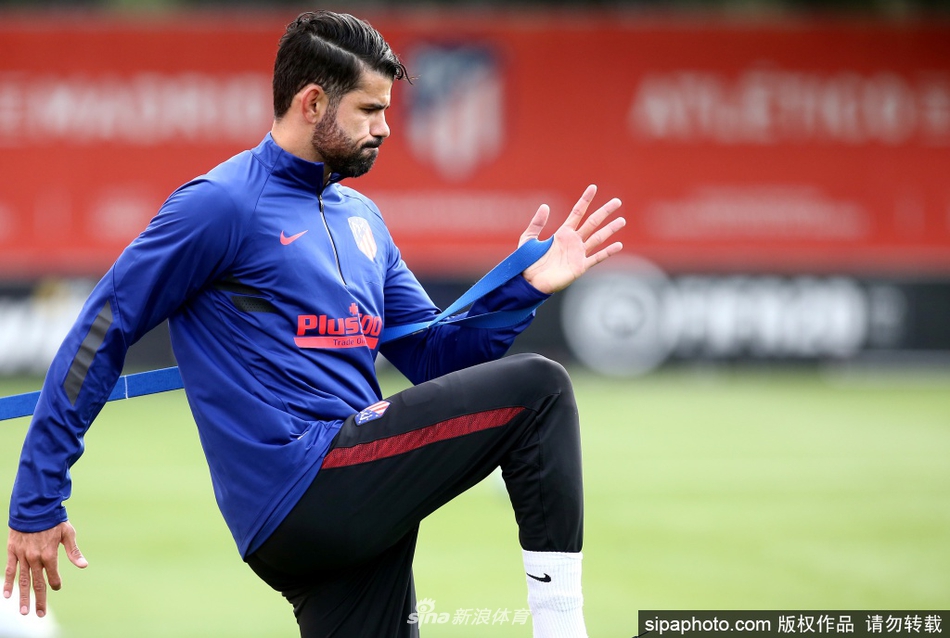 训练场上，一位球员正在做拉伸运动，他的动作舒展而有力，身后的蓝天白云与红色的训练服构成一幅充满活力的画卷。