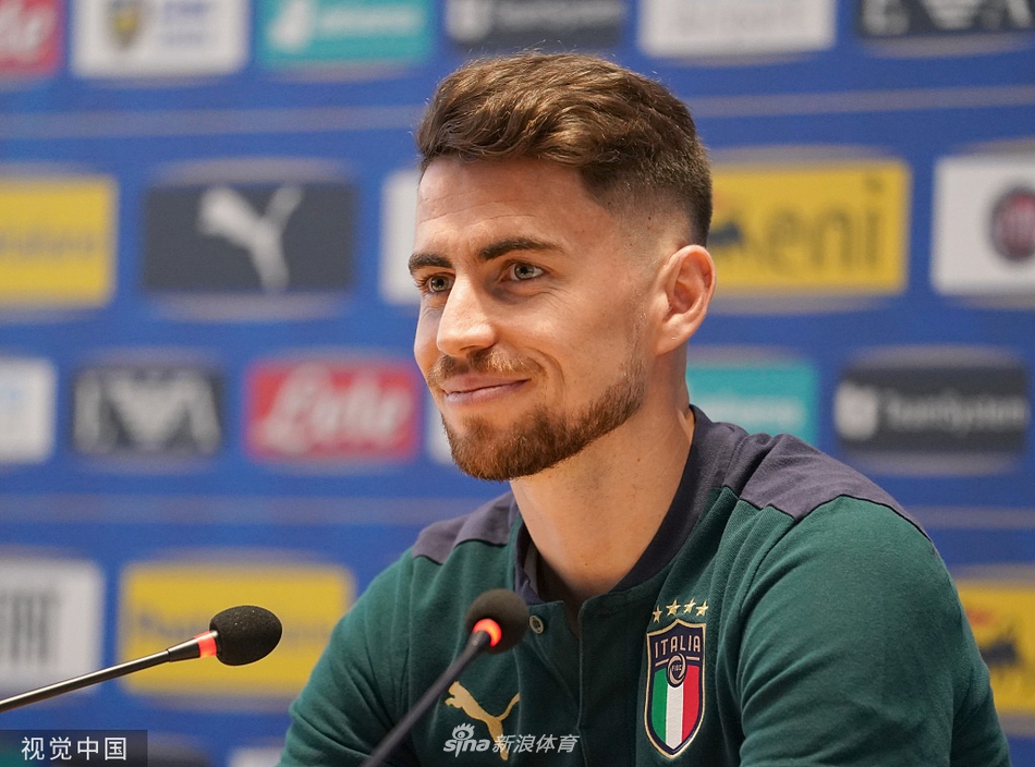 发布会进行到深入阶段，若日尼奥侧身专注聆听记者提问，微张的嘴唇和紧锁的眉头显示出他对问题的认真思考，桌上的话筒和品牌标识细节清晰可见。