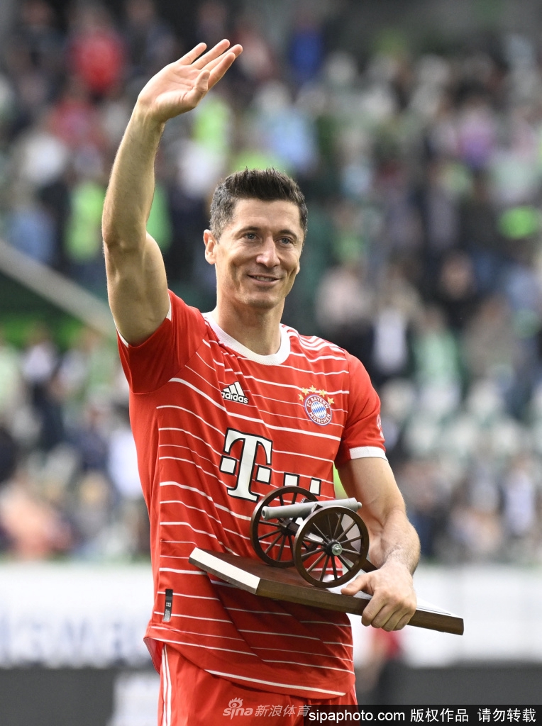 莱万多夫斯基手持金靴奖杯，目光坚定地望向远方，身后是绿茵场与看台，象征着荣誉与传奇的传承