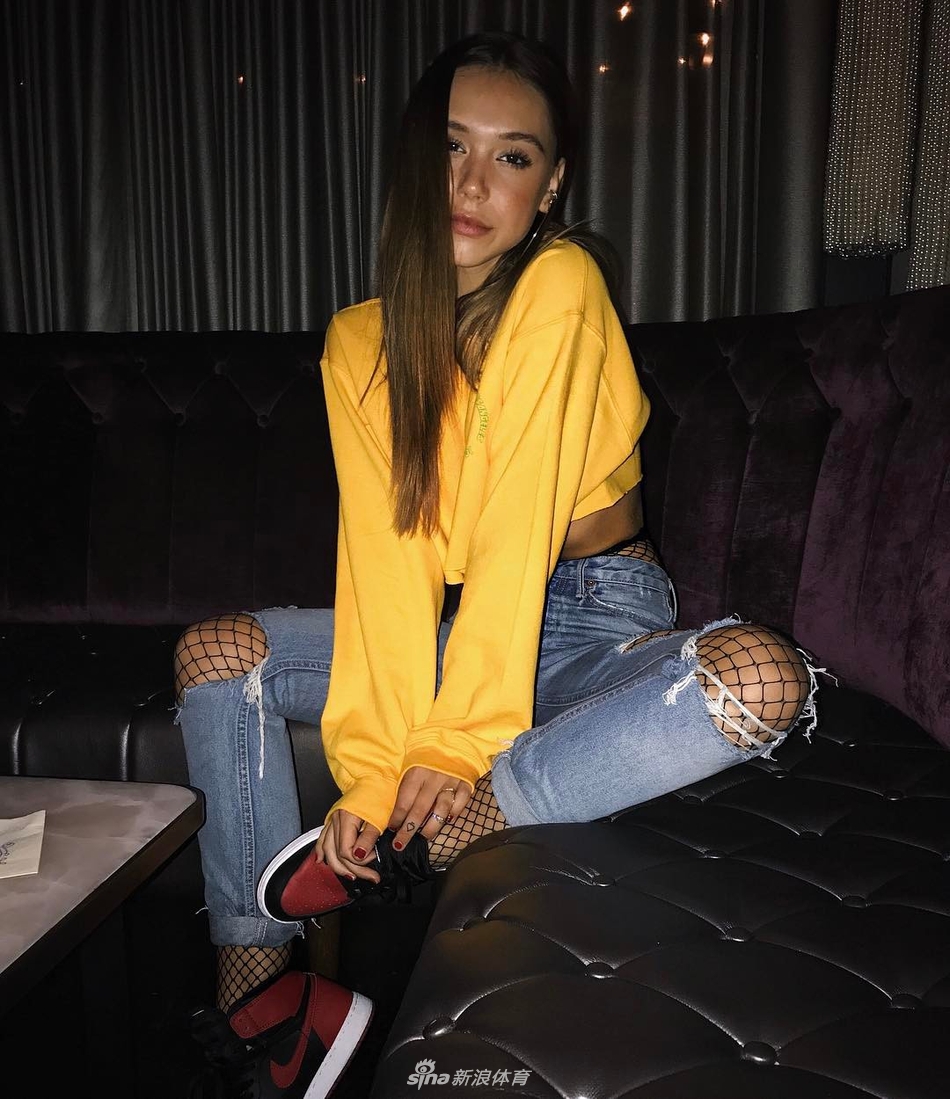 Alexis Ren身处洛杉矶的街头涂鸦墙前，她穿着高腰牛仔裤，上身是一件简约的白色Crop Top，露出紧实的马甲线，脚上的亮色AJ成为全身穿搭的焦点，尽显美式街头的随性与自信。