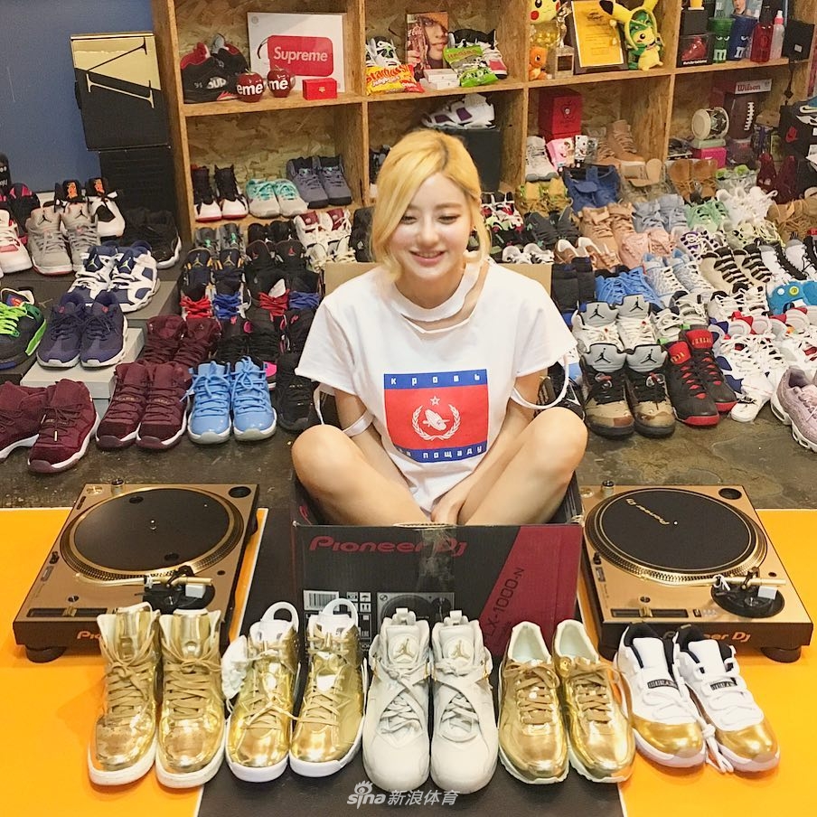 DJ Soda 半蹲在地上,身后是堆积如山的Nike与Jordan鞋盒,她穿着一袭白色连衣裙,金色的短发显得格外俏皮,眼神中透露出对自己收藏帝国的满足与骄傲。