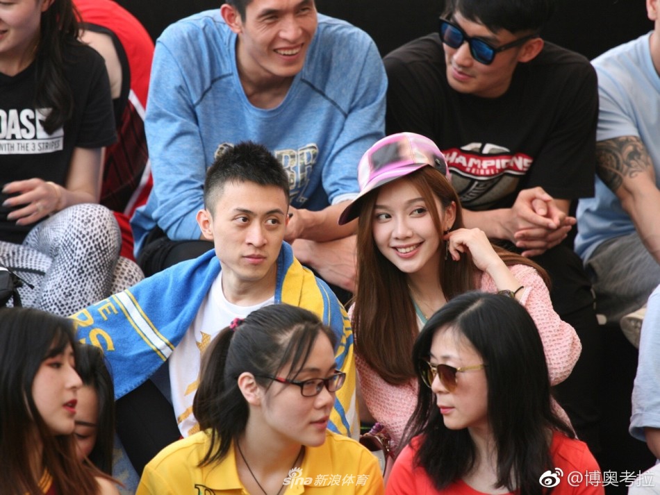 球馆通道内，秦奋身背双肩包，一手拿着手机，一手拿着饮料，神态轻松自然，仿佛只是一个普通的篮球爱好者刚刚看完一场精彩的比赛，准备离场。