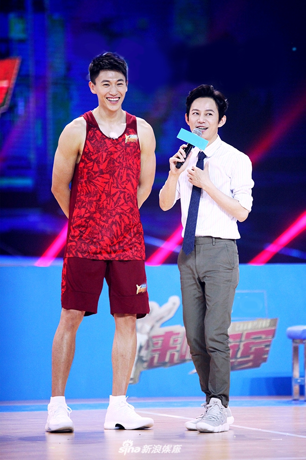 奥尼尔张开双臂试图阻拦开着移动篮筐小车的宋茜，巨大的体型差形成鲜明对比，场面欢乐如同大人与孩子的嬉戏