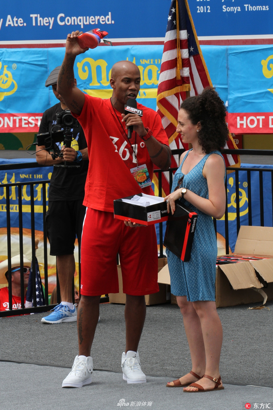 镜头拉近，马布里神情专注地看向比赛方向，左手下意识地指向自己胸前那个醒目的个人品牌商标，仿佛在告诉镜头后的观众：今天的主角除了热狗，还有我脚下的这双鞋。