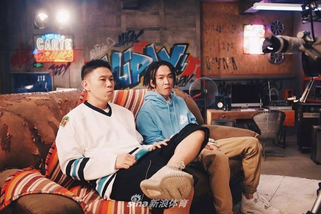 你的男孩TT身穿潮服，在涂鸦背景前活力四射，他脚上的Air Jordan 4 'Pure Money'白银配色干净利落，完美诠释了年轻Rapper的阳光与自信