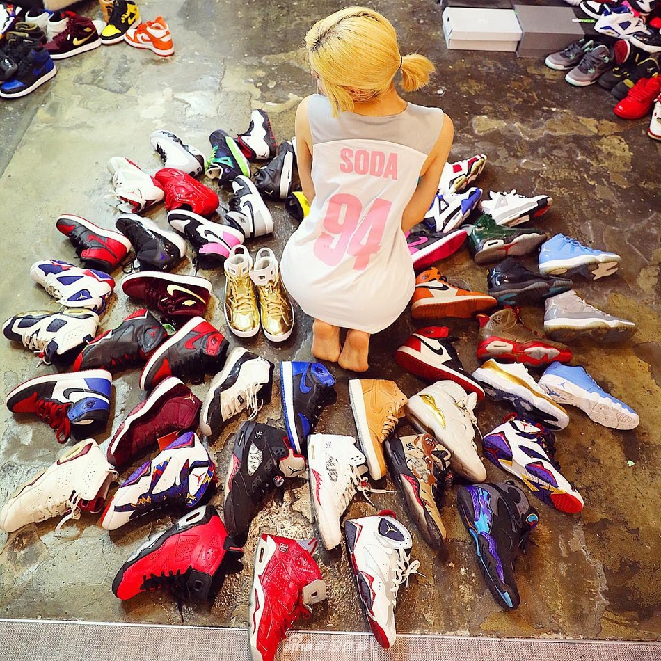 在暖色调的灯光下,DJ Soda坐在堆积如山的球鞋中间,她身穿黑色T恤和破洞牛仔裤,手里拿着一双球鞋仔细端详,身旁色彩斑斓的鞋盒仿佛是她最珍贵的宝藏库。
