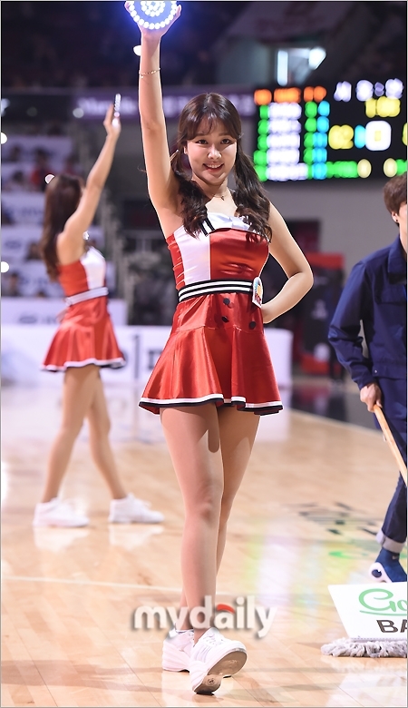 在中场休息的灯光下, 啦啦队员手持彩色花球, 以极具感染力的灿烂笑容面对观众, 展现出阳光健康的形象