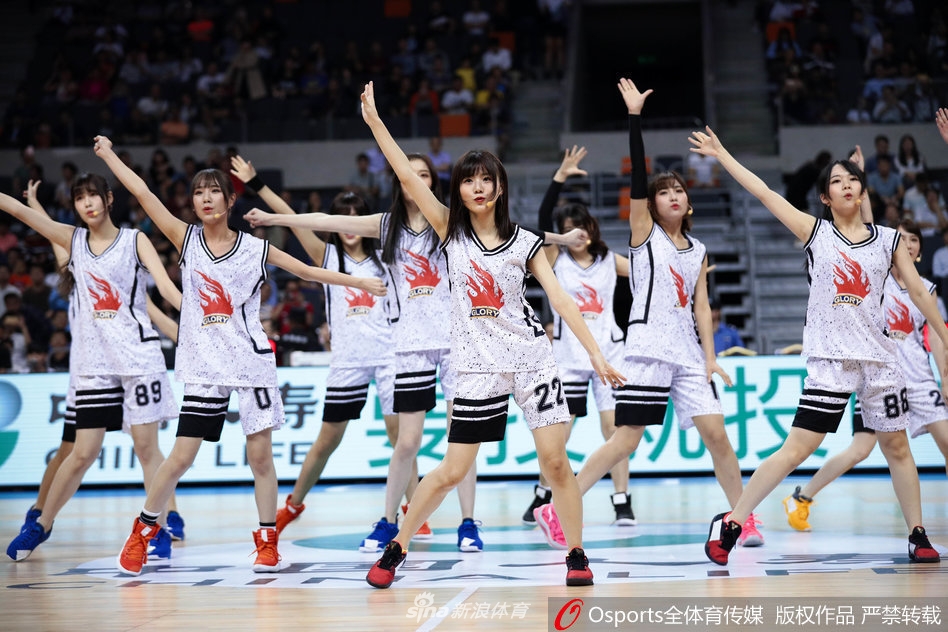 镜头特写一位GNZ48成员，她手持啦啦队花球，专注的眼神中透露出对舞台的热爱，背后是宏远主场巨大的LED屏和热情的观众席。