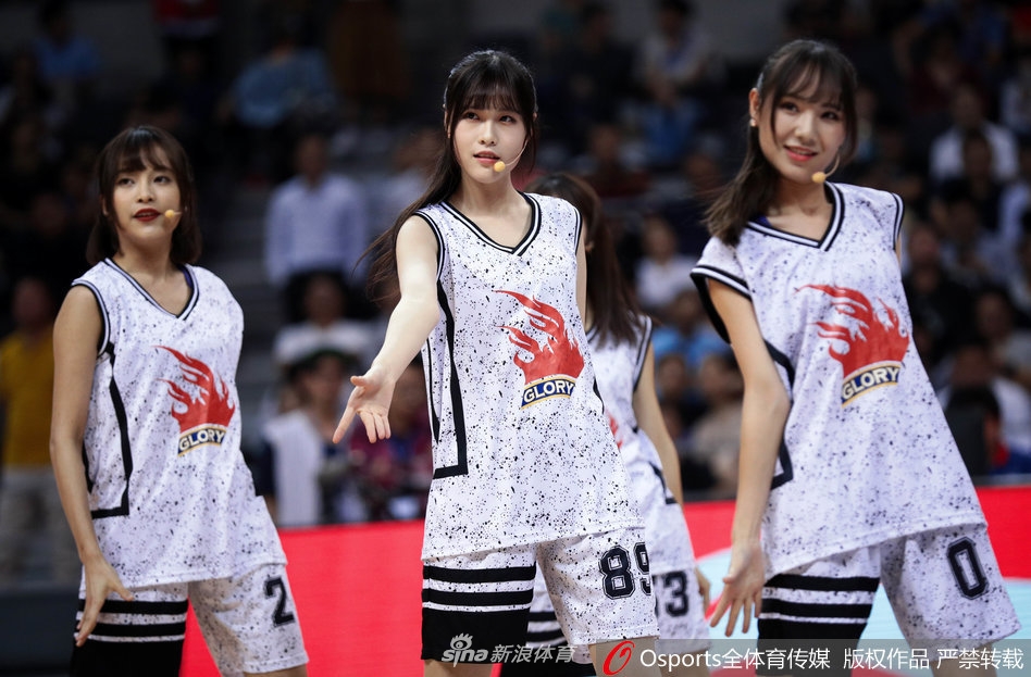 一名GNZ48成员在赛场边回眸一笑，长发飘飘，身着紧身球衣勾勒出青春的身形，与身后专注观赛的球迷形成有趣的互动画面。