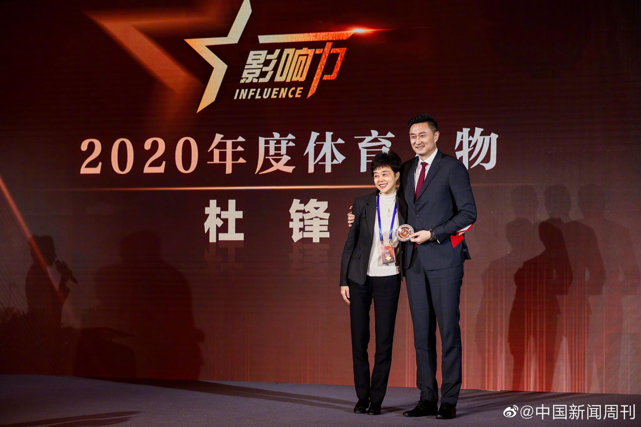 杜锋在颁奖典礼现场手捧奖杯,神情庄重而谦逊,背景是闪耀的聚光灯
