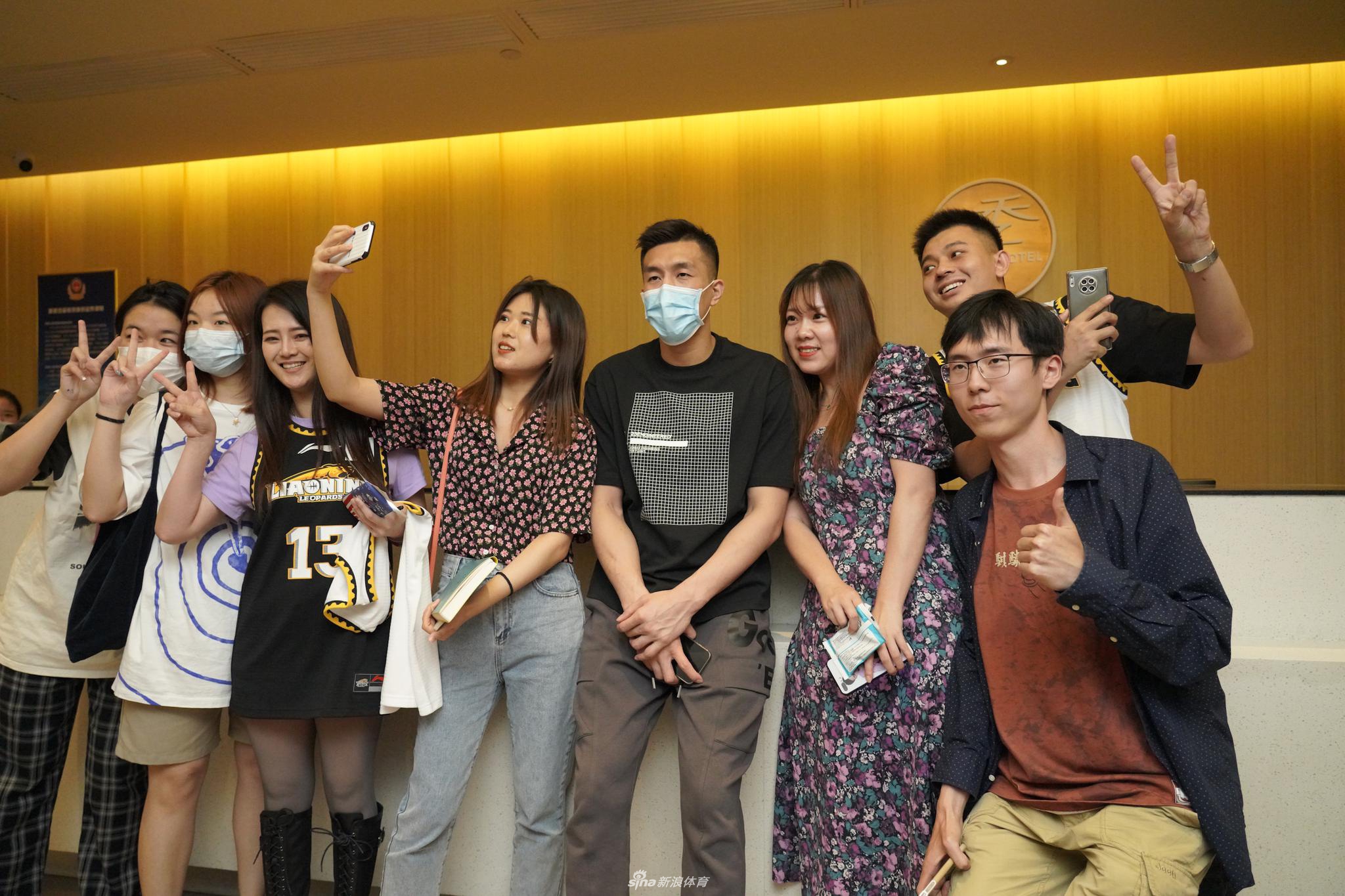 郭艾伦侧身对着镜头比出胜利的手势，身旁的女粉丝们举着手机争相拍摄，这一刻的欢乐被永久定格。