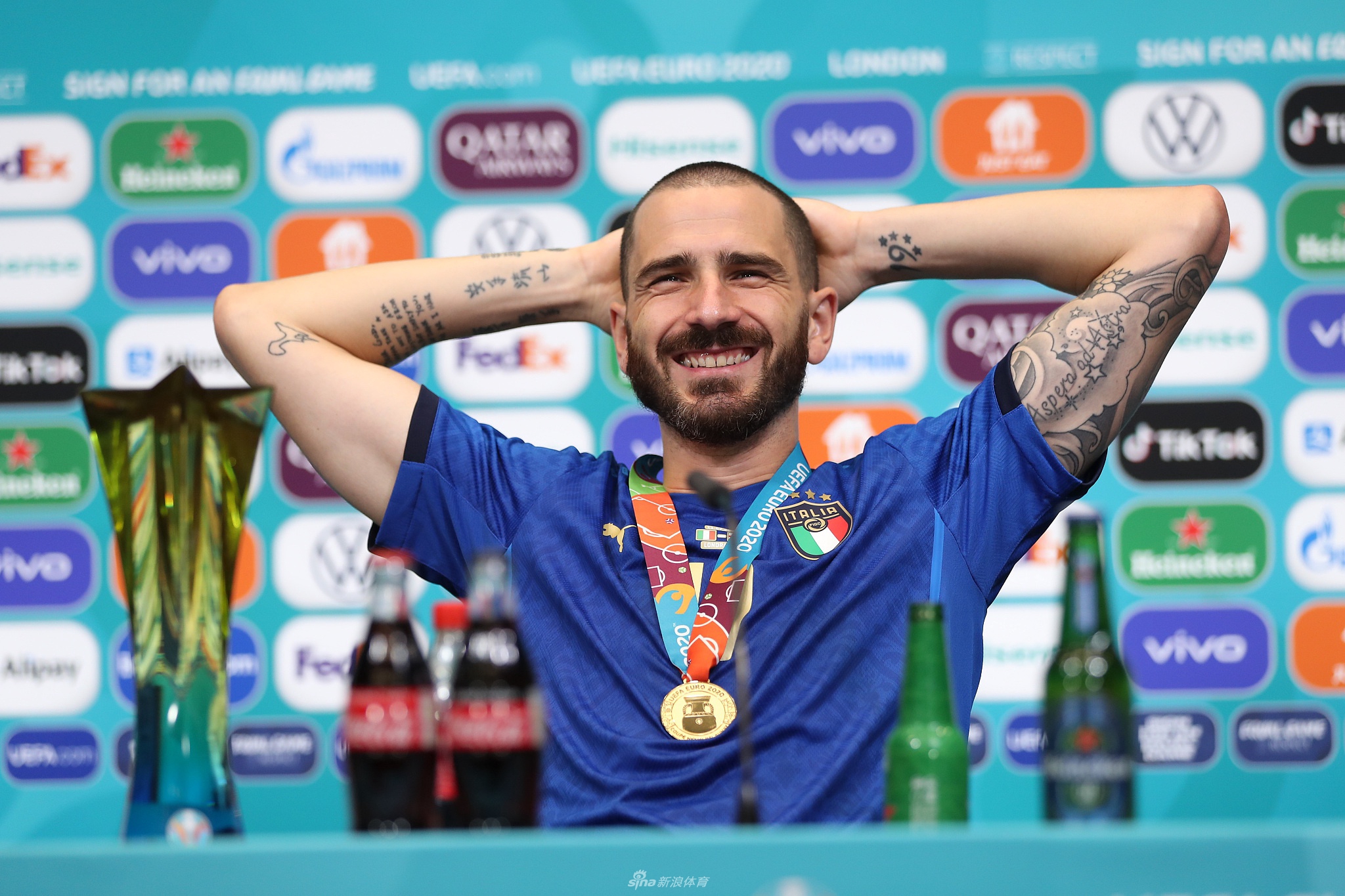 博努奇面前摆着已经喝了一半的啤酒和可乐瓶，他双手扶住桌沿，面带微笑地准备回答记者提问，神态轻松自如。