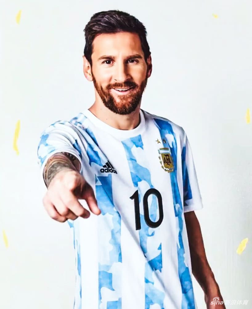 在柔和的光晕下，迪巴拉双手轻捧胸前徽章，神情专注而虔诚。新球衣蓝白条纹间的迷彩纹理显得尤为立体，仿佛他捧起的不是一块布料，而是整个阿根廷足球的厚重历史与未来希望。
