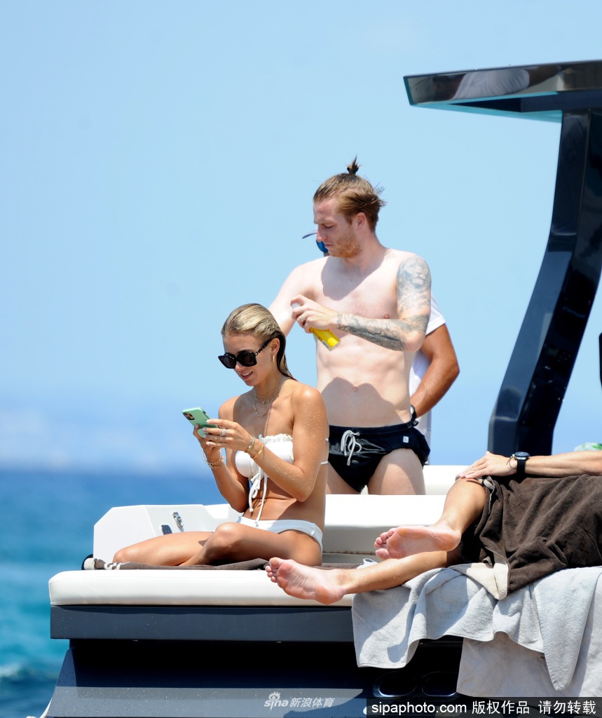 碧海蓝天之间，罗伊斯赤裸上身展示精壮肌肉，身旁的斯嘉丽身着纯白比基尼，古铜色肌肤在阳光下熠熠生辉，两人相视而笑，甜蜜气息几乎要溢出屏幕