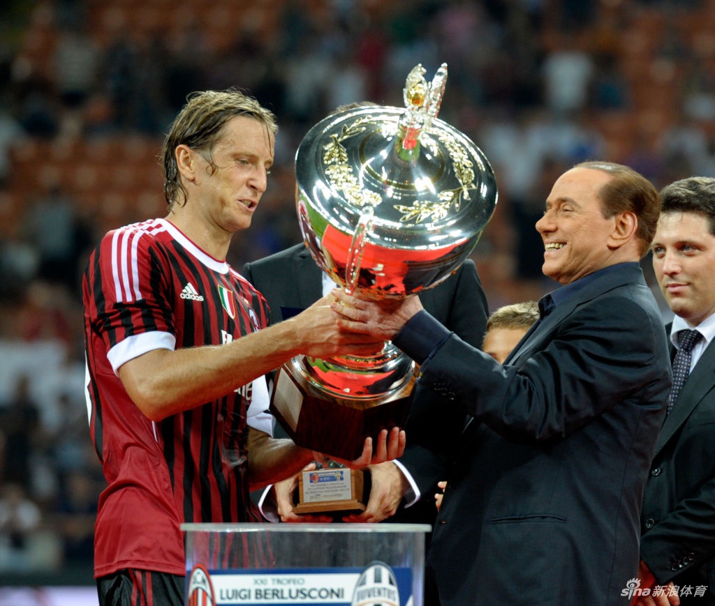 贝卢斯科尼面带标志性的微笑，在米兰家中宽敞的客厅里签署一份文件，茶几上摆放着他与家人的合影，背后是巨大的书架，透露出即便隔离也不停歇的工作节奏