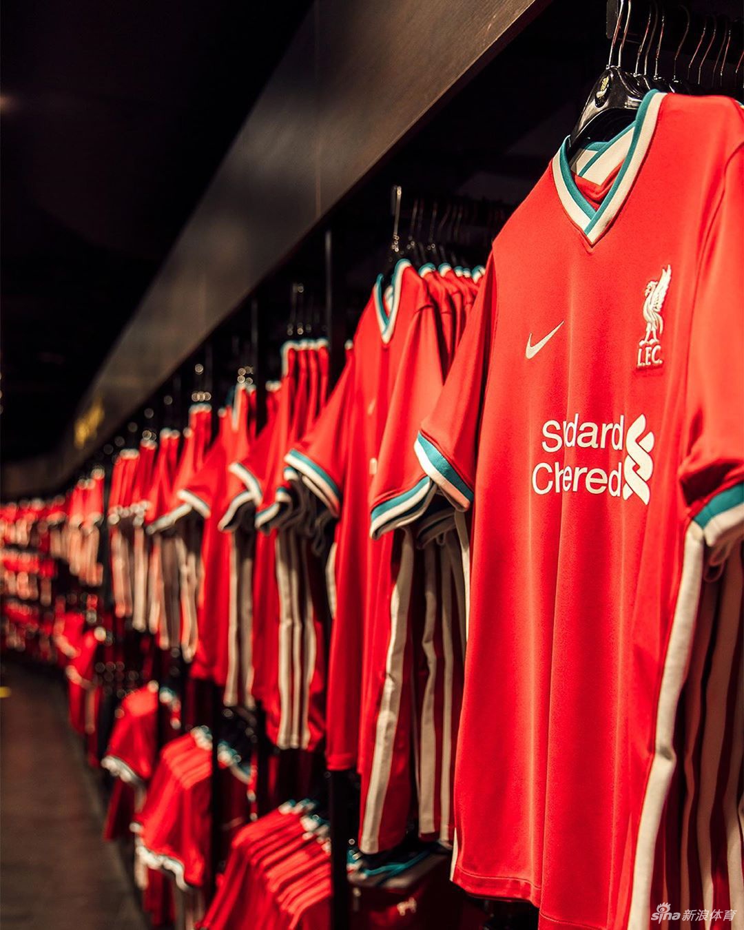 模特身穿全套全新主场球衣在球场边展现英姿，全身红色的搭配充满视觉冲击力，白色的球衣细节与水鸭绿条纹在奔跑中划出优美的线条，完美诠释了现代足球的时尚感与运动美学。