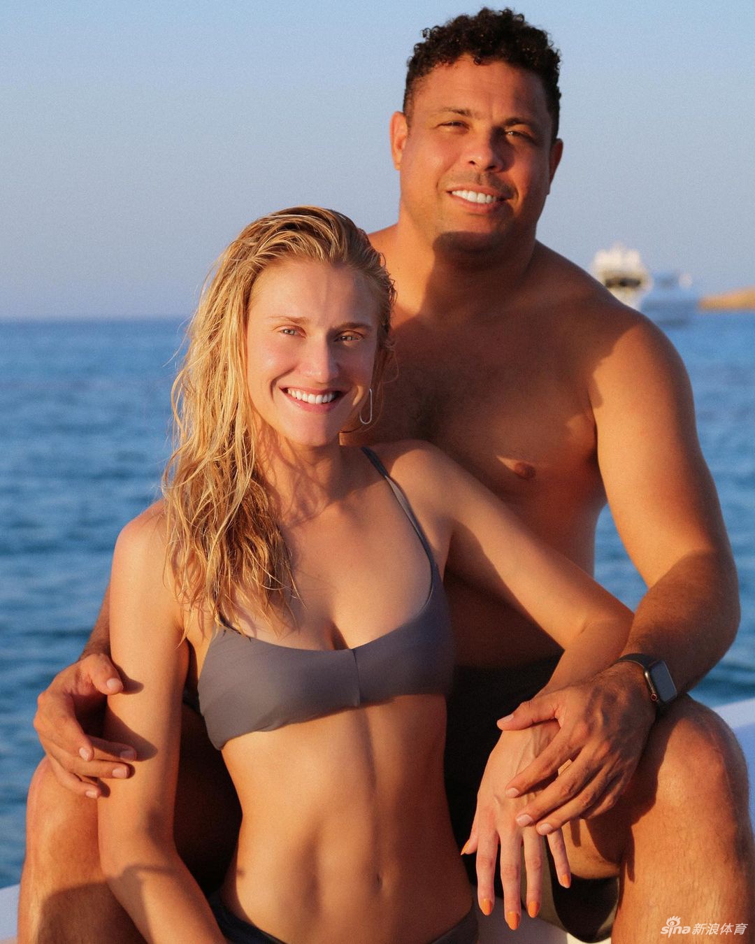 赛琳娜穿着休闲的白色T恤，坐在沙发上，怀里抱着一件小小的婴儿连体衣，脸上抑制不住地流露出即将成为母亲的激动与喜悦